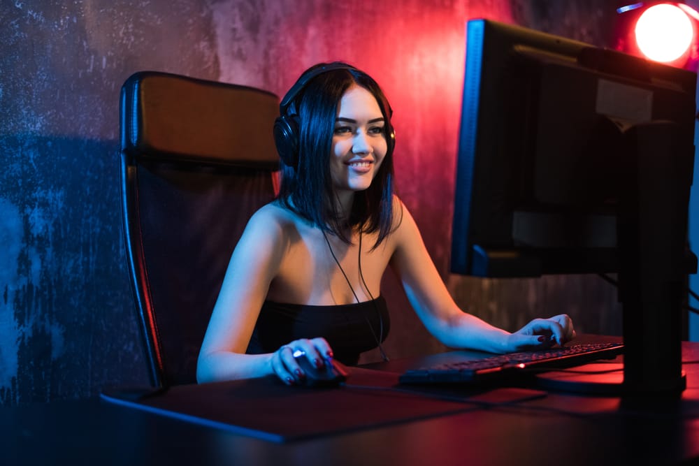 A Cute Female Gamer Girl Sits In A Cozy Room Behind A Computer And Plays Games. Woman Live Streaming Computer Video Games To Her Fans. Streamer And Gamer Concept